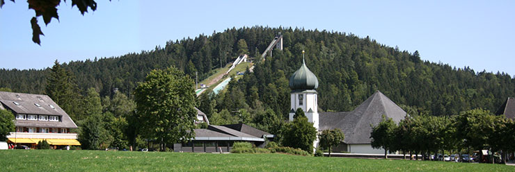 Skisprungzentrum Hinterzarten mit Zwiebelturmkirche im Vordergrund